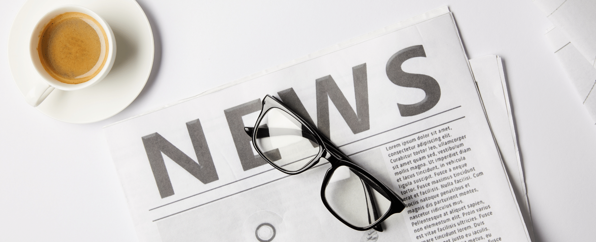 News written on newspaper with black rimmed glasses on top and next to a cup of coffee cup filled with coffee