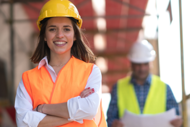 young woman in a construction hat smiling while she builds her tiny house on wheels