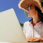 young woman in a hat working an online job at the beach