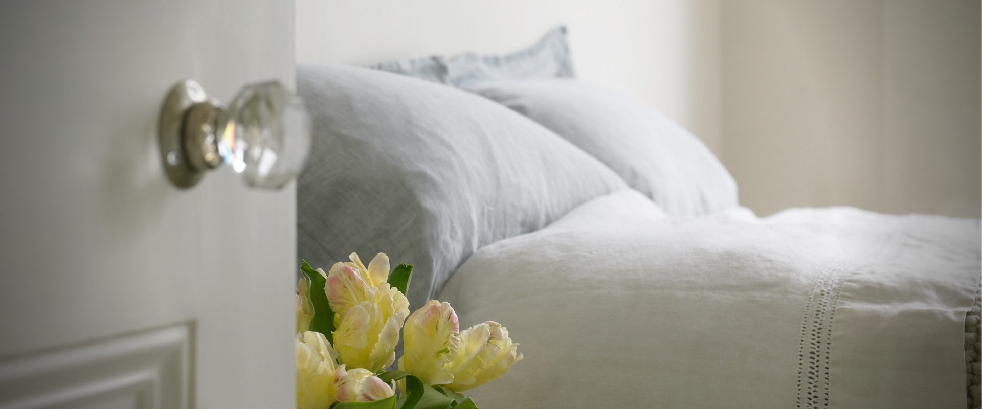 host home bed in white linens and a vase of yellow flowers