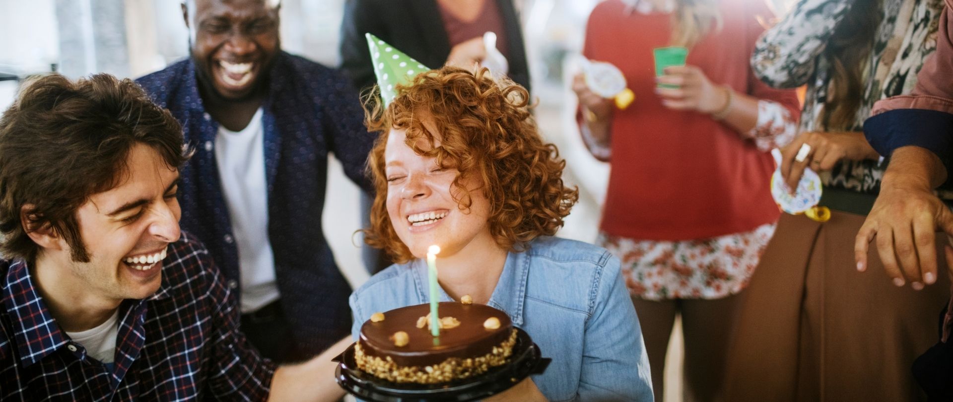 young lady with a birthday cake and candle surrounded by friends