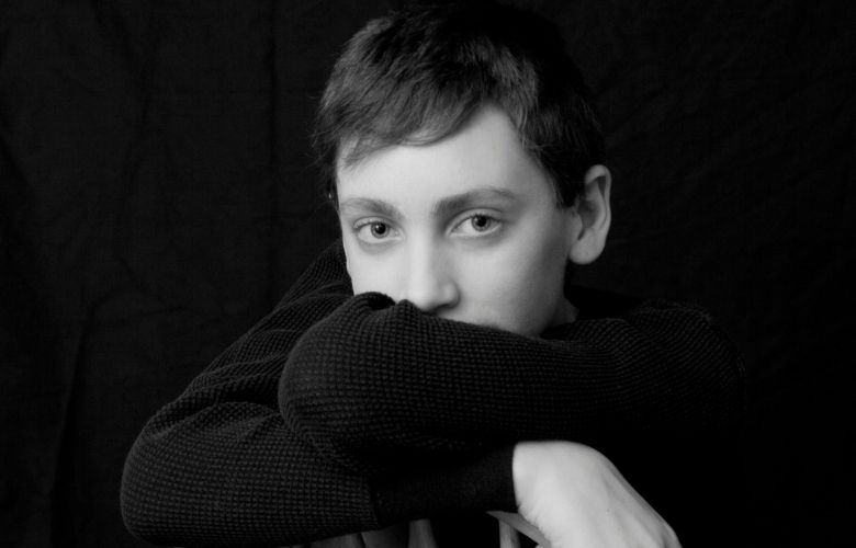 teenage boy hiding behind crossed arms in a black sweater